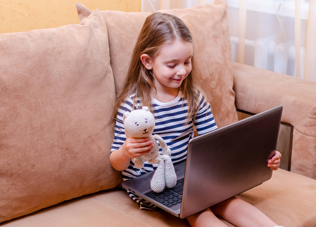 Mały dzieciak online z wideo rozmowy nauczyciela. Szczęśliwa dziewczynka uczy się, komunikuje zdalnie. Spójrz na laptopa i bądź zaskoczony. Uczenie się na odległość. komunikacja internetowa - Zdjęcie, obraz