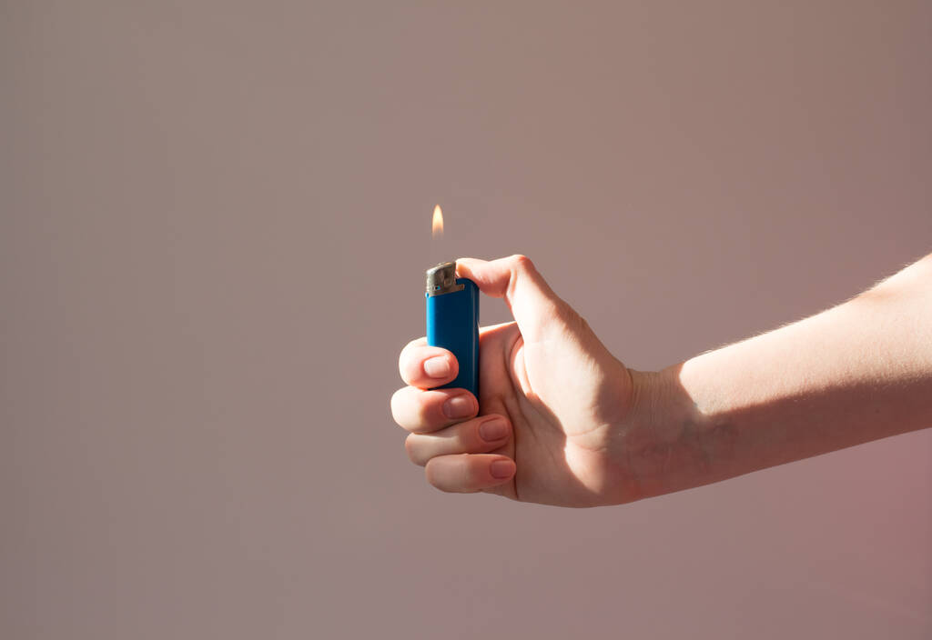 Quemaduras más ligeras en la mano a la sombra. Un hombre sostiene un encendedor con una llama. Incendio y fumar concepto
 - Foto, Imagen