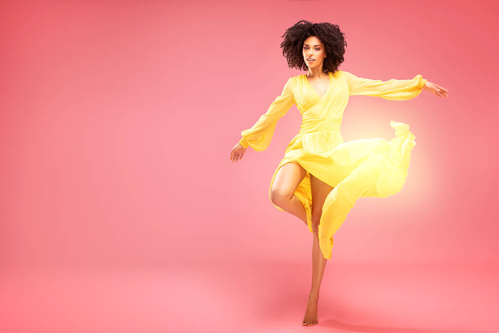 Афро-молода жінка танцює в жовтій сукні максі над рожевим пастельним студійним фоном
. - Фото, зображення