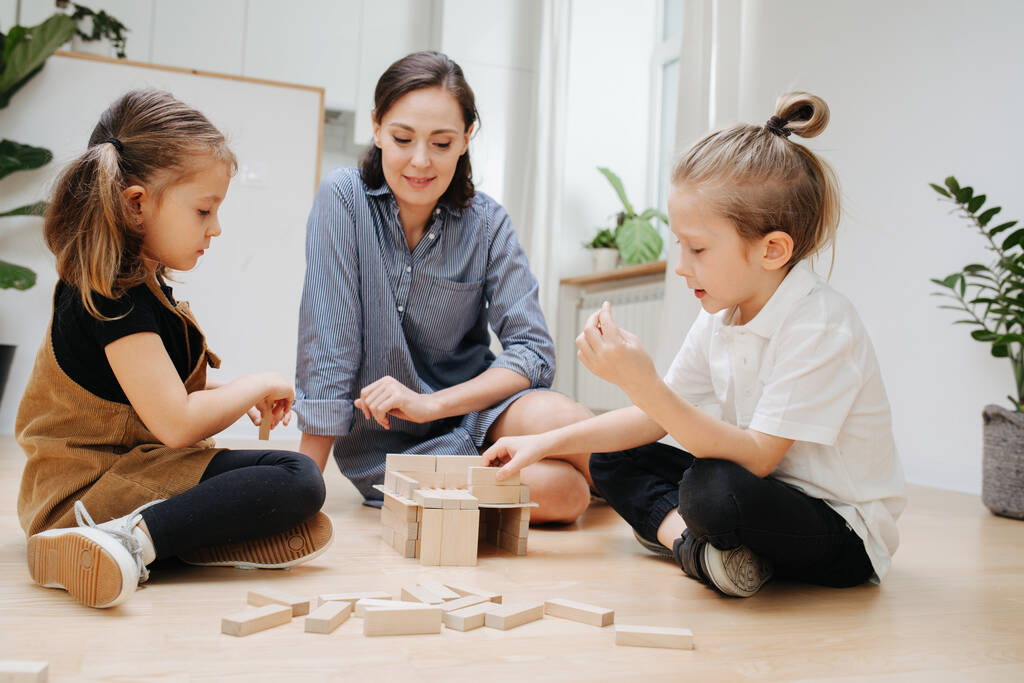Máma a děti si hrají s dřevěnými bloky, stavějí jednoduchý dům během izolace doma. - Fotografie, Obrázek