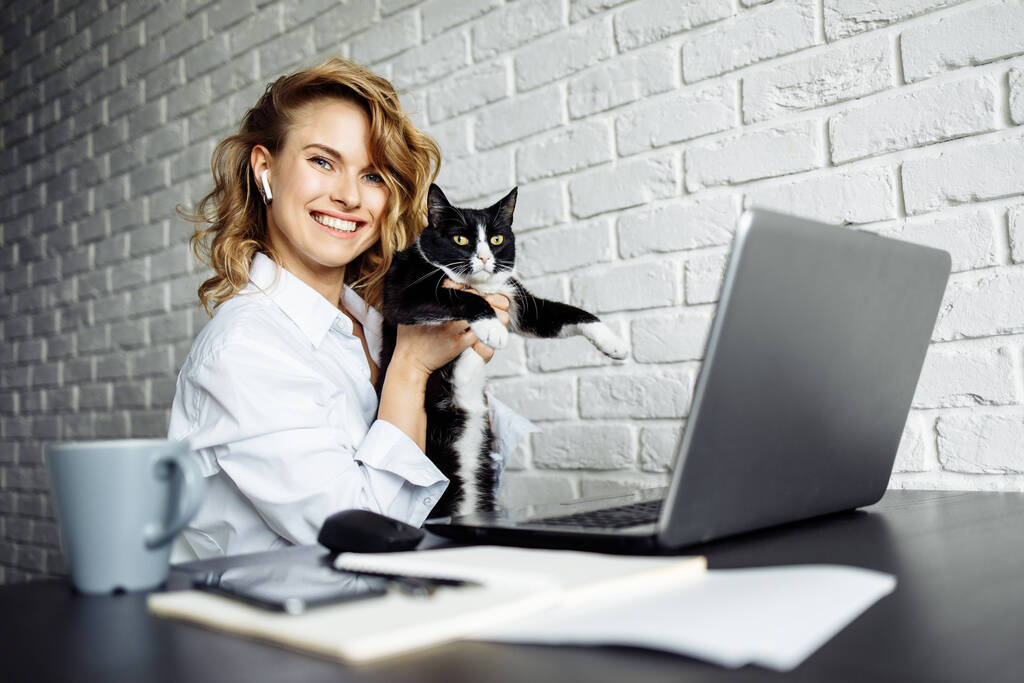Glückliche Frau mit schwarzer Katze im Arm, die mit Laptop am Tisch sitzt. - Foto, Bild