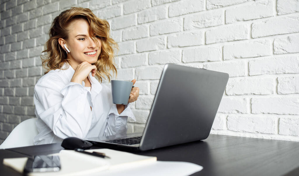 Uśmiechnięta kobieta z kręconymi włosami siedząca przy stole z laptopem. - Zdjęcie, obraz