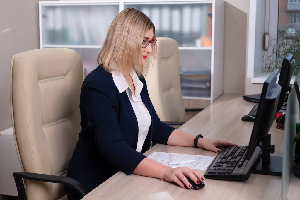 眼鏡をかけた若い金髪の女はサラリーマン。女性はテーブルに座ってコンピュータで仕事をしています. - 写真・画像