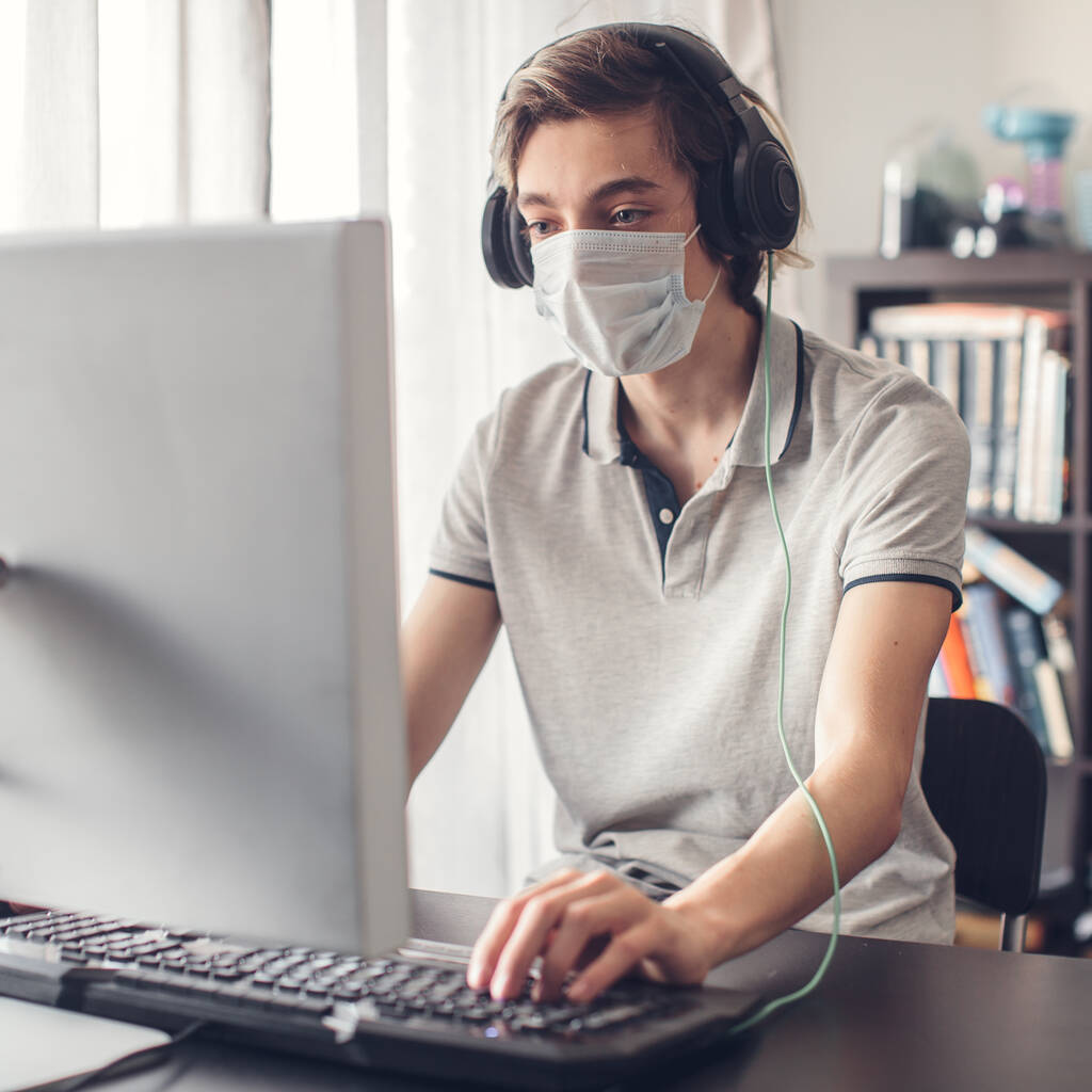 Teenager spielen zu Hause mit Computer und tragen Schutzmaske - Foto, Bild