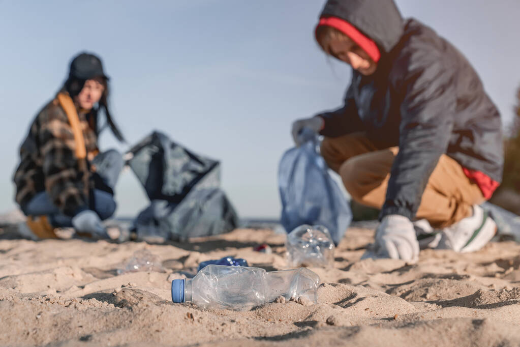 Plastikler plajda ve arka planda bir grup gönüllü var. Ön plandaki plastiğe odaklan - Fotoğraf, Görsel