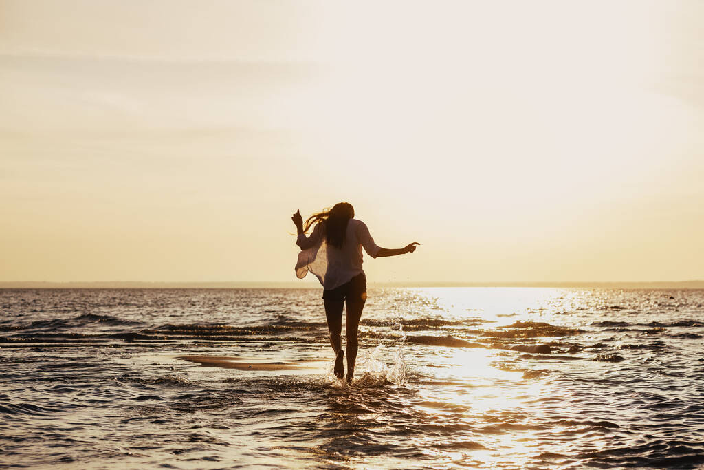 Slim dziewczyna spacery przez zachód słońca plaży w wodzie - Zdjęcie, obraz