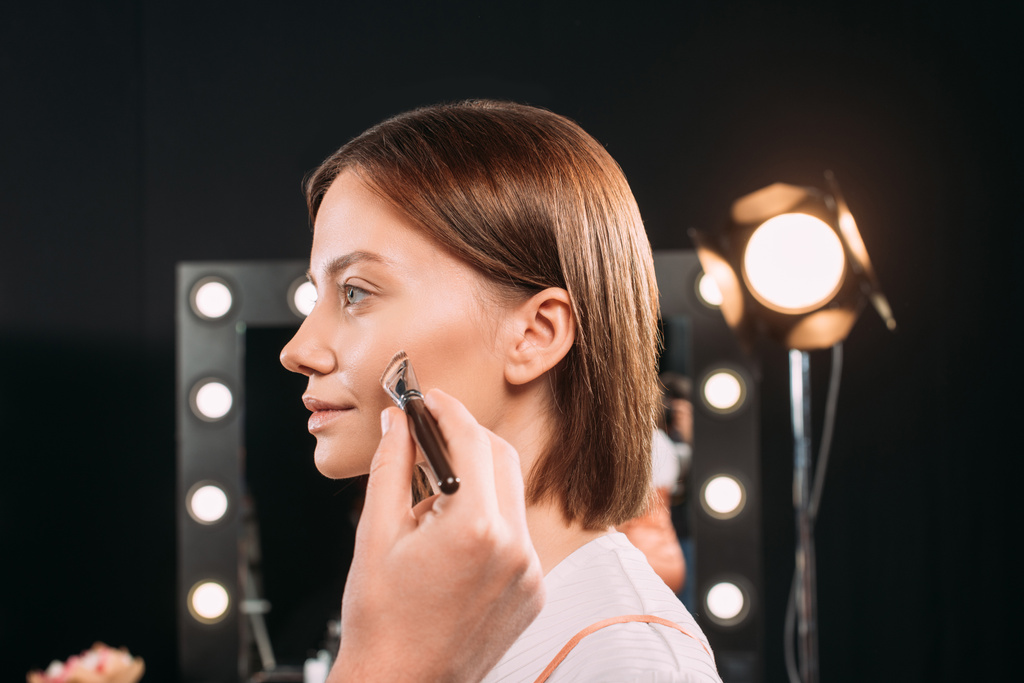Sminkes gazdaság kozmetikai kefe közelében arc gyönyörű modell fotó stúdió  - Fotó, kép
