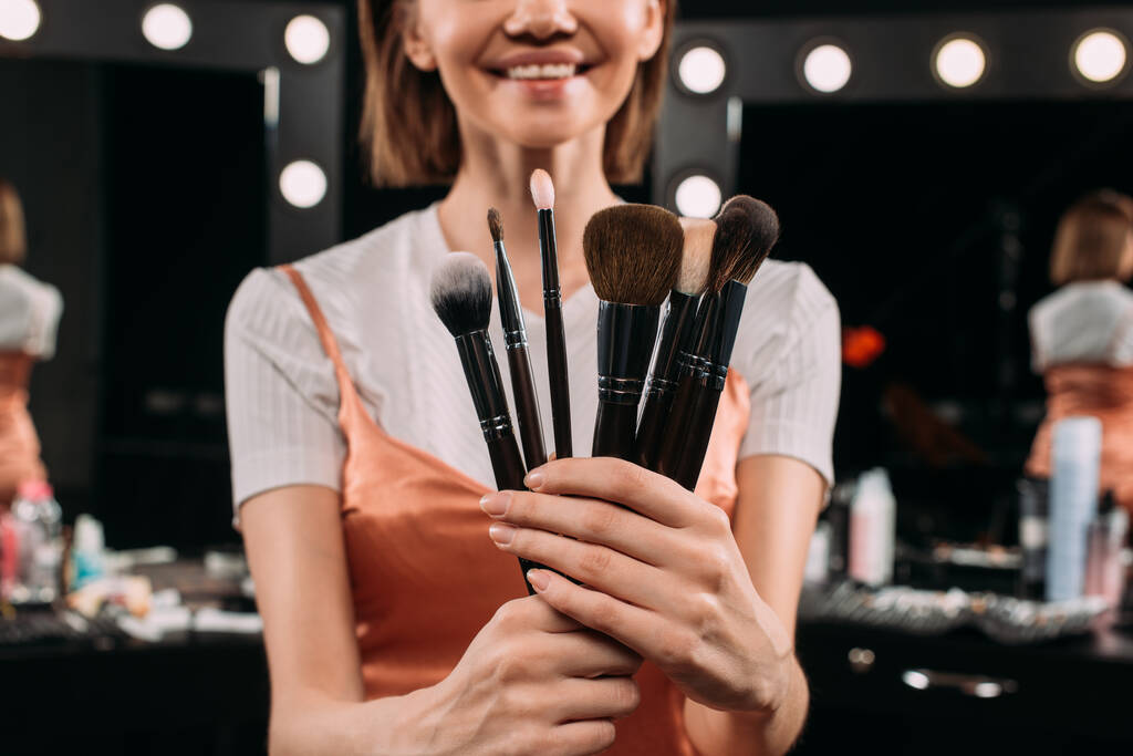 Foco seletivo de mulher sorridente segurando escovas cosméticas no estúdio de fotos
  - Foto, Imagem
