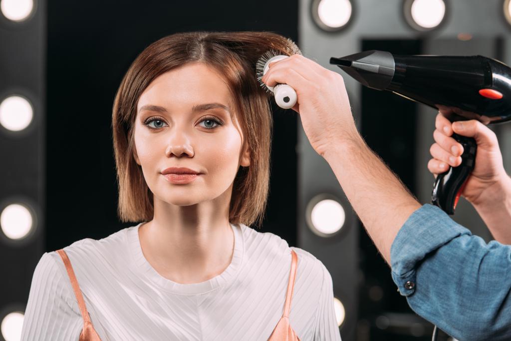 Makyöz, saç fırçası ve saç kurutma makinesiyle çekici bir kadına saç stili yapıyor.  - Fotoğraf, Görsel