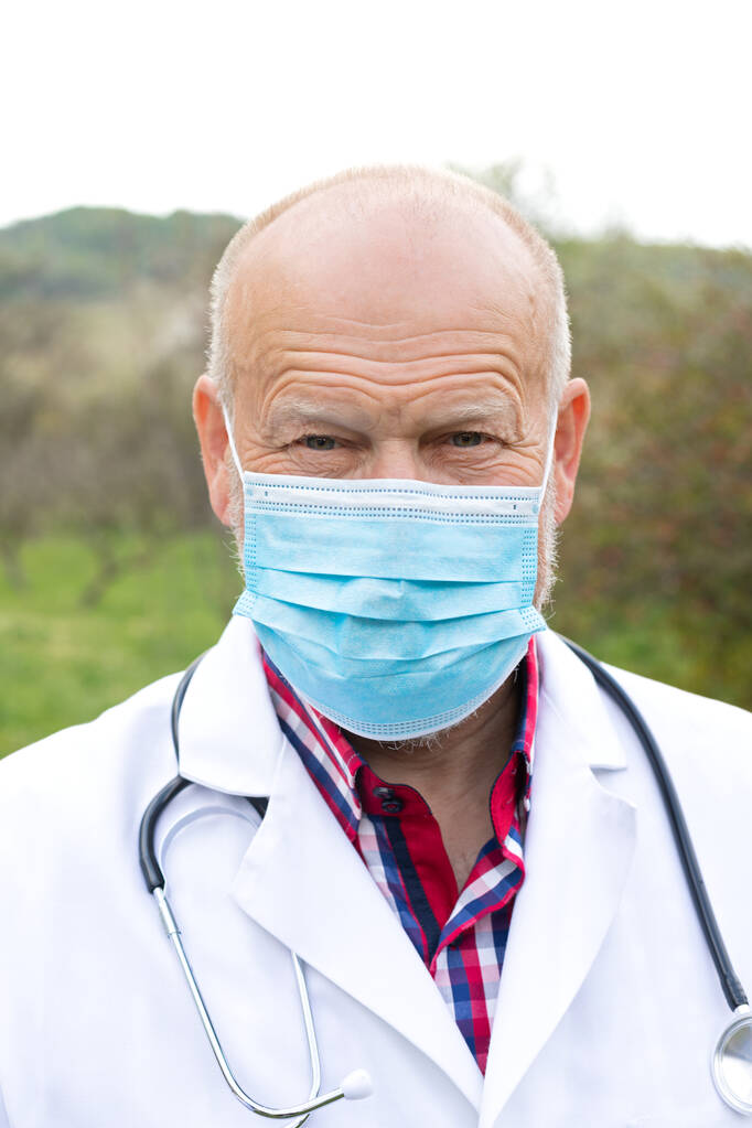 Portrait de médecin masculin senior avec uniforme et masque chirurgical posant à l'extérieur
 - Photo, image