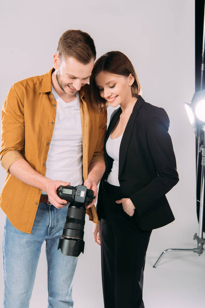 Fotógrafo guapo y hermosa mujer sonriente mirando la pantalla de la cámara digital en el estudio de fotos
  - Foto, imagen