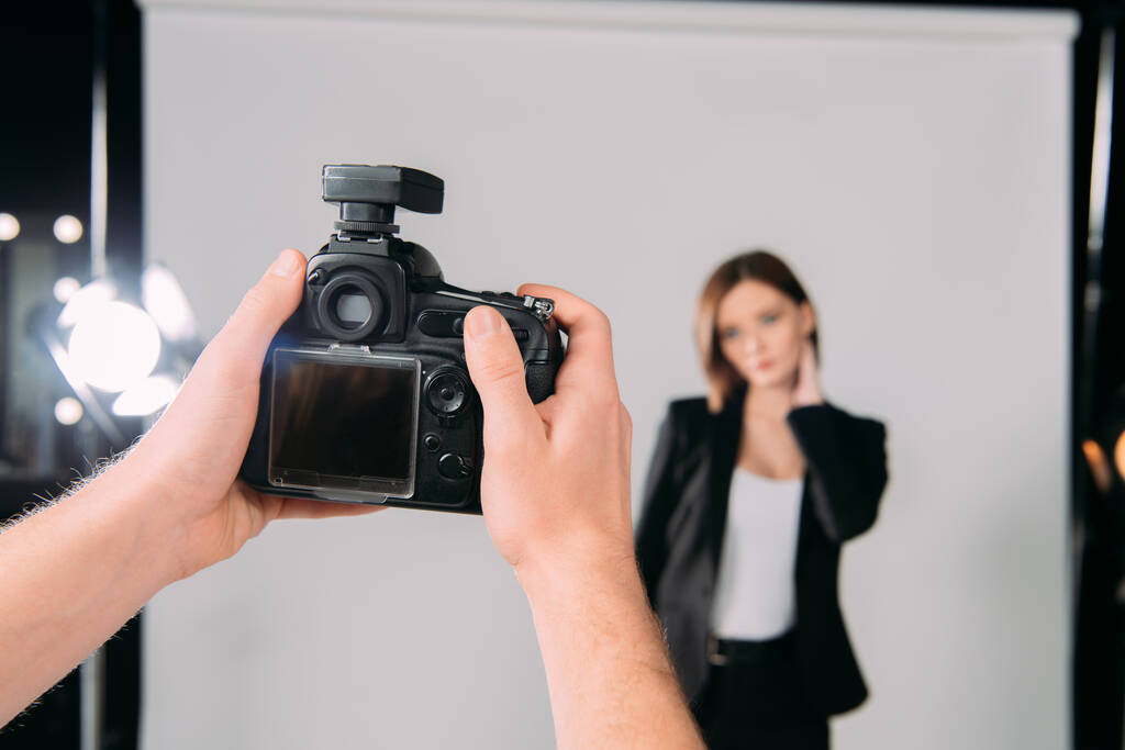 Selectieve focus van fotograaf met digitale camera in de buurt van model in fotostudio  - Foto, afbeelding