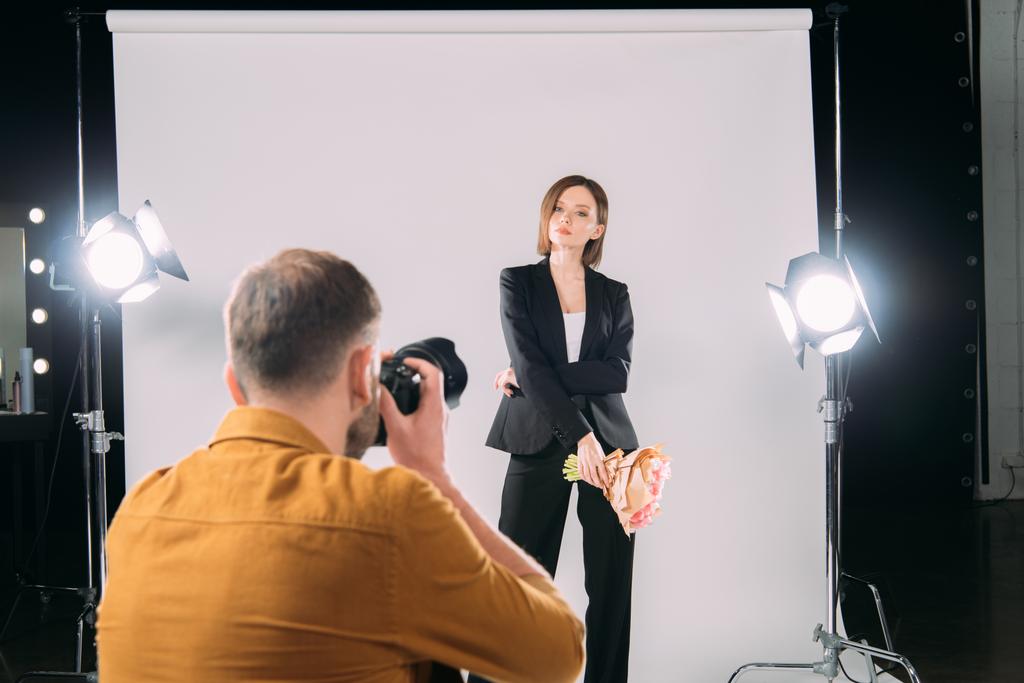 El foco selectivo del modelo de estilo con el ramo posando al fotógrafo con la cámara digital en el estudio fotográfico
  - Foto, Imagen