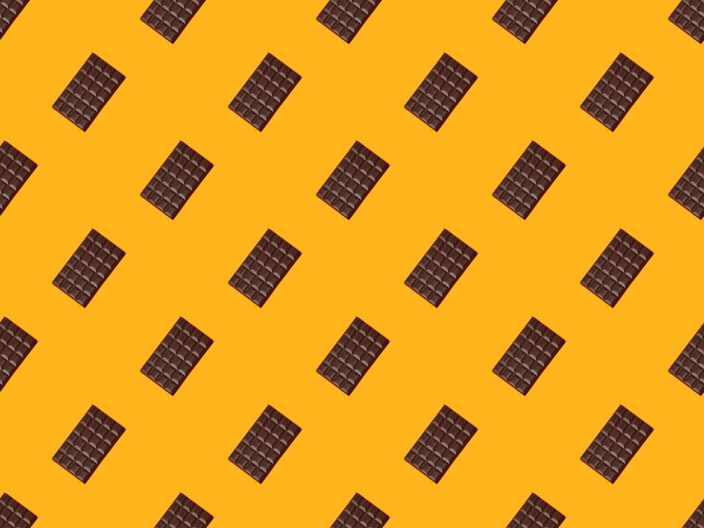 Draufsicht auf süße dunkle Schokoladentafeln auf orangefarbenem Hintergrund, nahtloses Muster - Foto, Bild