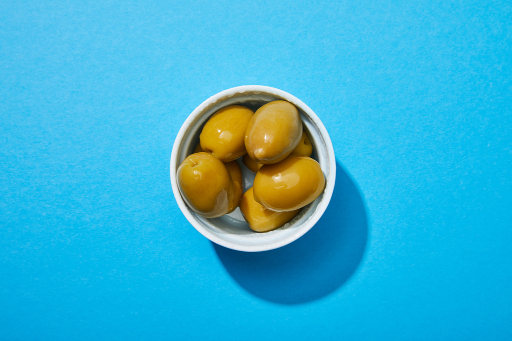 вид сверху на оливки в миске на голубом красочном фоне
 - Фото, изображение