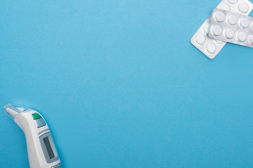 top view tabletták buborékcsomagolásban és infravörös hőmérő kék háttér - Fotó, kép