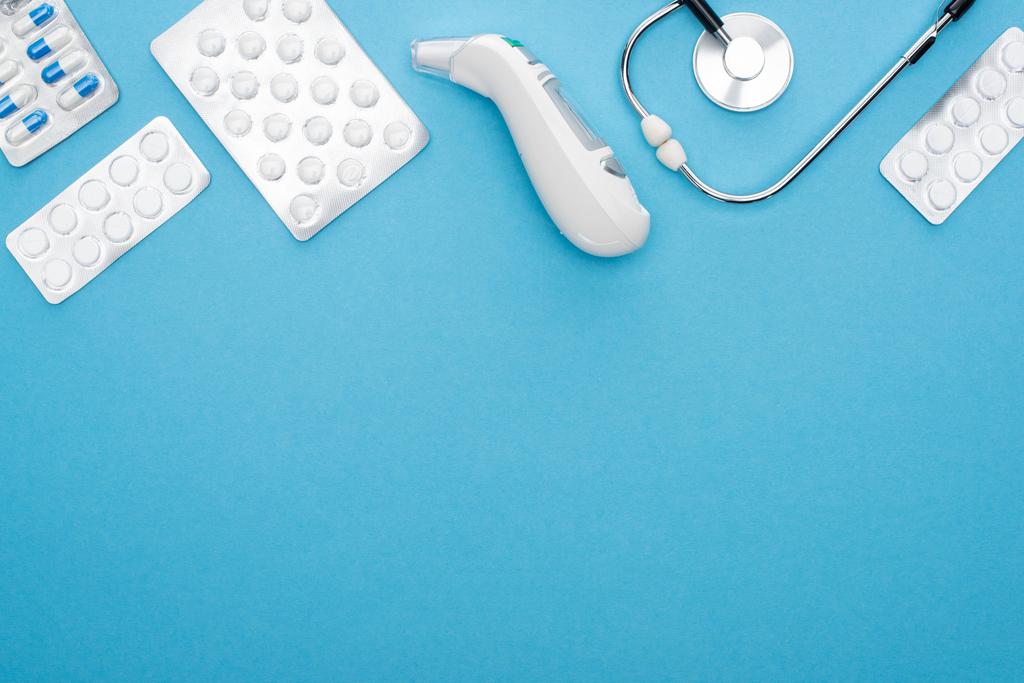 top view tabletták buborékcsomagolásban, sztetoszkóp és fül hőmérő kék háttér, vízszintes kép - Fotó, kép