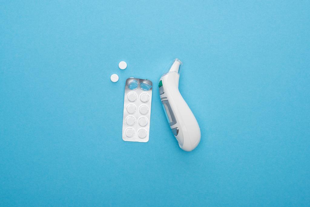 Ansicht von Pillen in Blisterverpackung und Ohrthermometer auf blauem Hintergrund - Foto, Bild