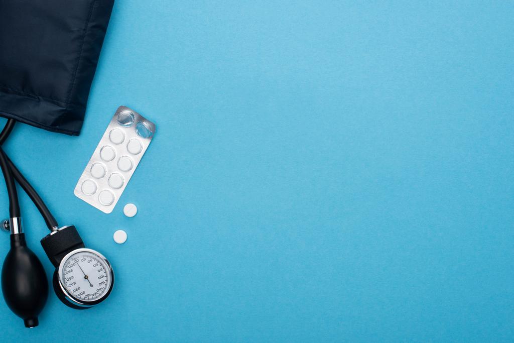 horní pohled na pilulky v blistrech balení, sfygmomanometr na modrém pozadí - Fotografie, Obrázek
