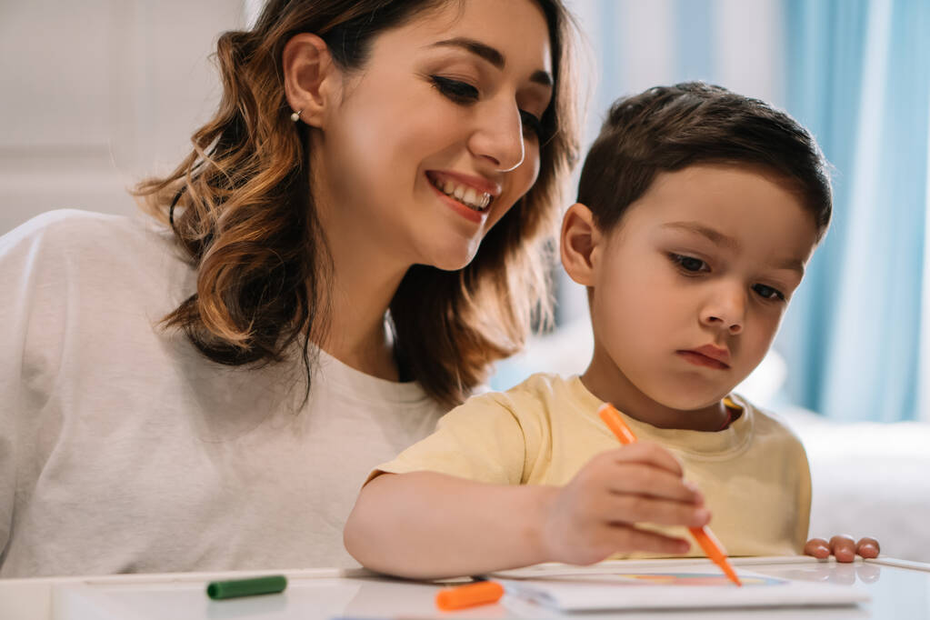 веселая мать смотрит на очаровательного сына рисует с войлочной ручкой
 - Фото, изображение