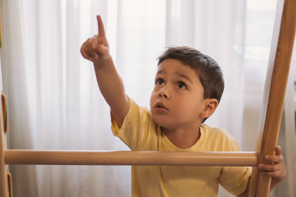 χαριτωμένο αγόρι δείχνοντας με το δάχτυλο, ενώ αγγίζοντας σκάλα του γυμναστηρίου στο σπίτι - Φωτογραφία, εικόνα