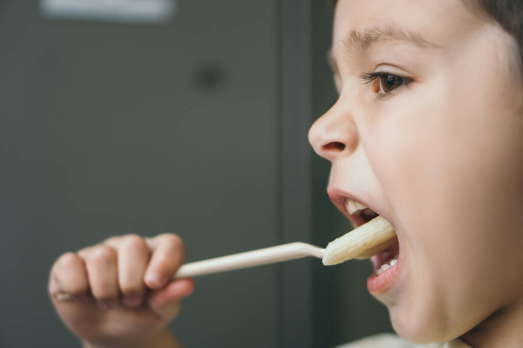 πλαϊνή άποψη του αξιολάτρευτο αγόρι έχοντας δείπνο, ενώ τρώει ζυμαρικά με πιρούνι - Φωτογραφία, εικόνα