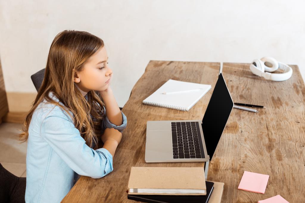 zijaanzicht van kind op zoek naar laptop met leeg scherm tijdens online studeren thuis  - Foto, afbeelding