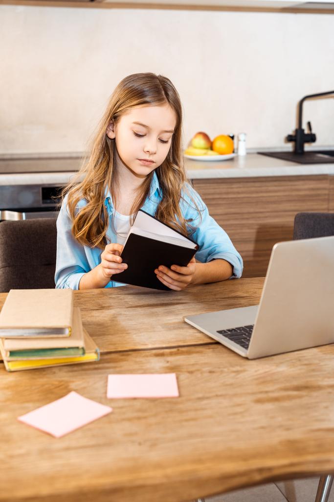 вибірковий фокус дитини, що тримає книгу біля ноутбука під час онлайн-навчання вдома
 - Фото, зображення