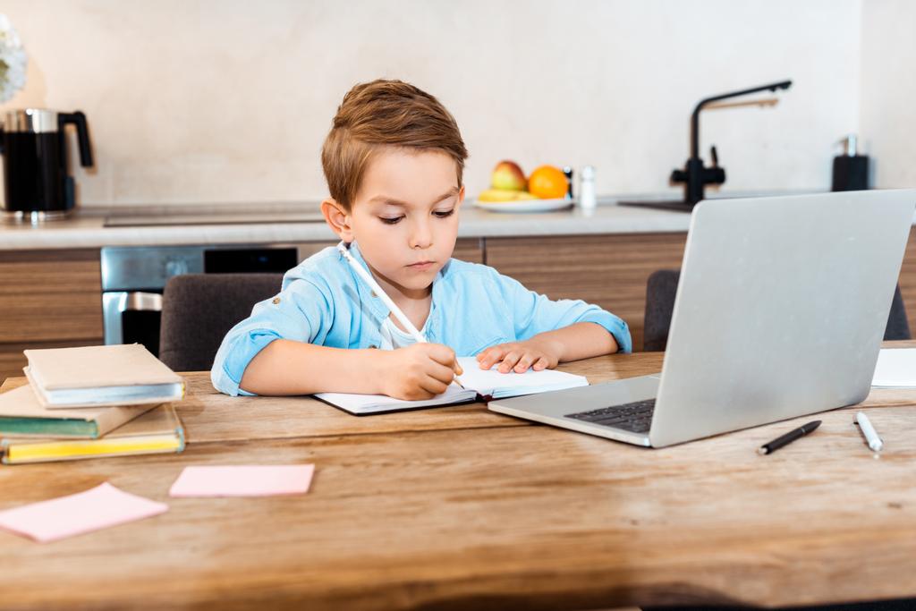 enfoque selectivo de la escritura del niño en el cuaderno cerca de la computadora portátil, mientras que el e-aprendizaje en casa
 - Foto, imagen