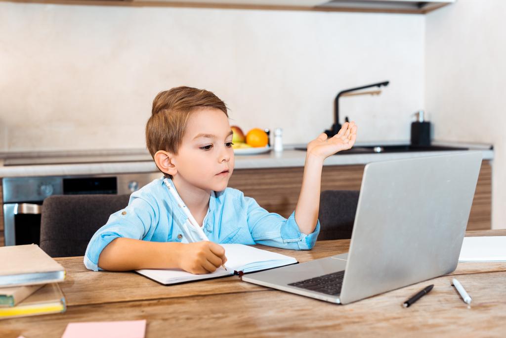 селективное внимание мальчика, который пишет в блокноте и смотрит на ноутбук во время электронного обучения дома
 - Фото, изображение