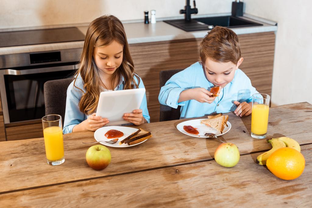 garçon manger pain grillé avec confiture près de soeur en utilisant une tablette numérique
  - Photo, image