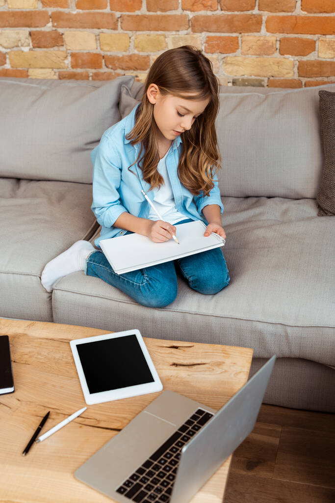 enfant heureux assis sur le canapé et écrire dans un ordinateur portable près de gadgets
  - Photo, image
