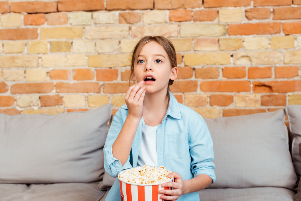 Überraschtes Kind schaut Film und hält Eimer beim Popcorn essen  - Foto, Bild