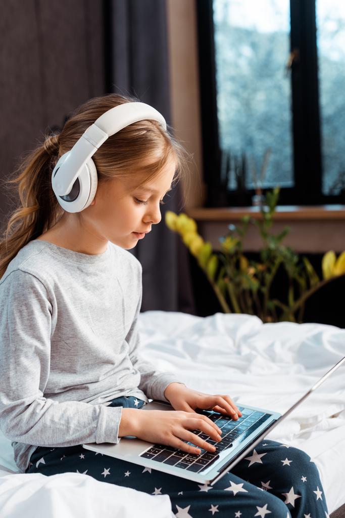 дитина в бездротових навушниках використовує ноутбук з електронним навчанням у спальні
  - Фото, зображення