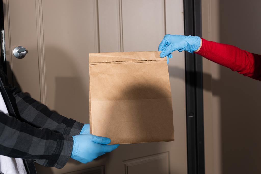 Vista recortada del repartidor hombre dando paquete a la mujer en guante de látex cerca de la puerta abierta
  - Foto, Imagen