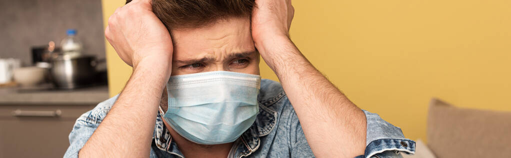 Panoráma termés stresszes férfi orvosi maszk néz el otthonról  - Fotó, kép