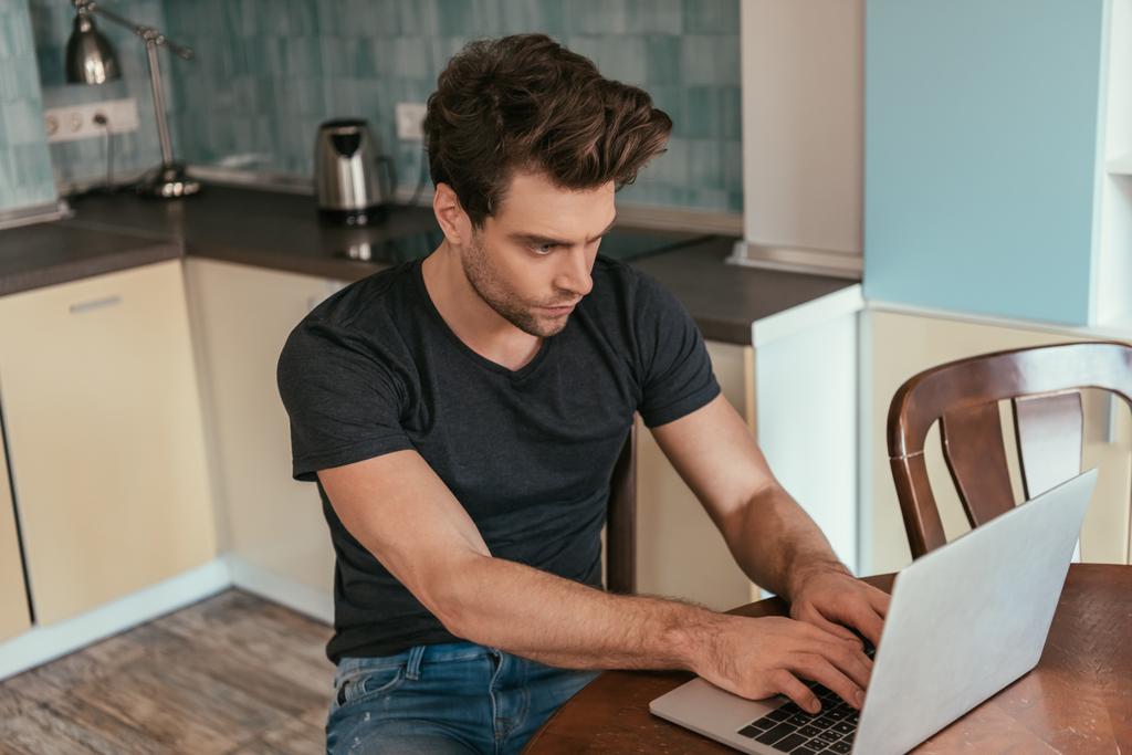 koncentrált férfi fekete pólóban dolgozik laptop otthon - Fotó, kép