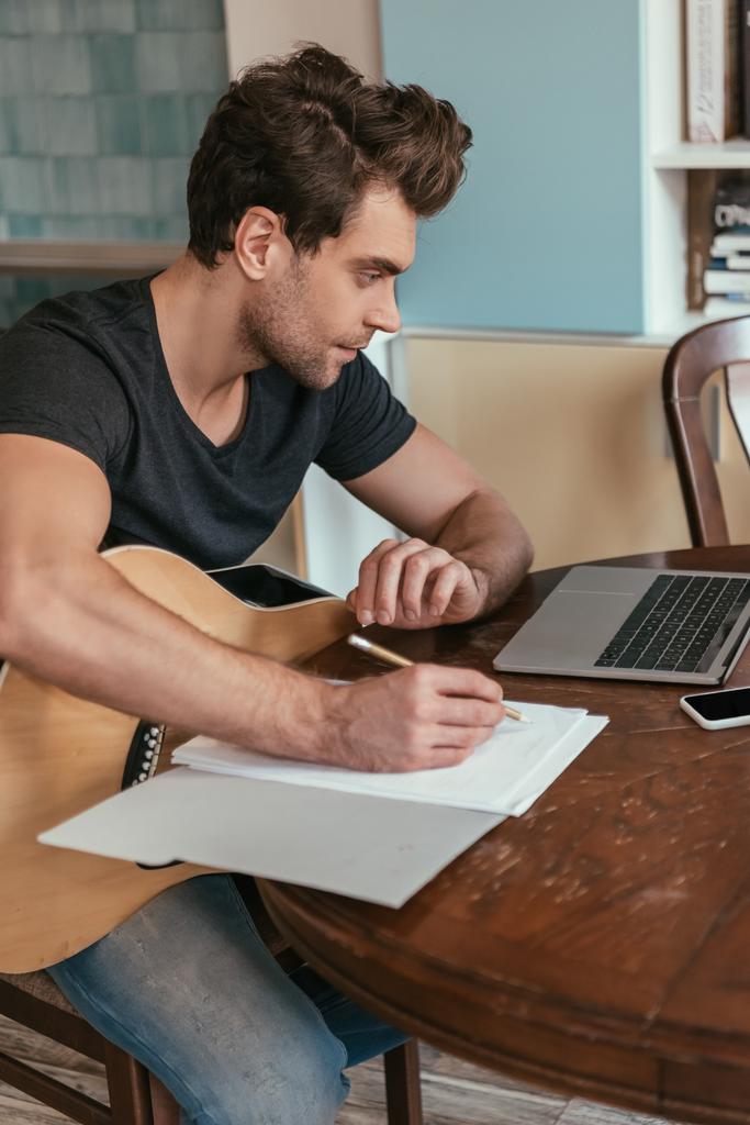 jovem concentrado com notas de escrita de guitarra enquanto olha para laptop
 - Foto, Imagem