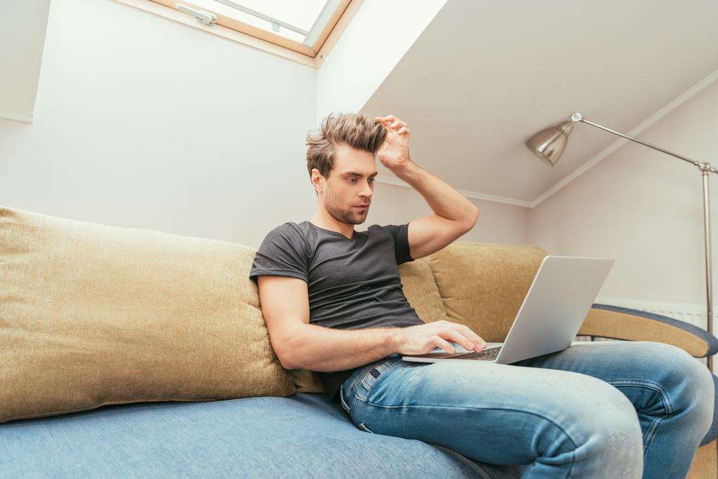 figyelmes fiatalember megérinti fejét, miközben dolgozik laptop otthon - Fotó, kép