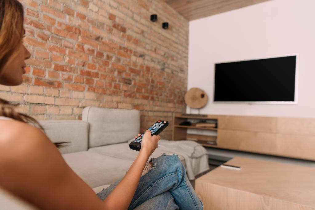 young woman holding remote controller and watching tv with blank screen during self isolation, selective focus - Photo, Image