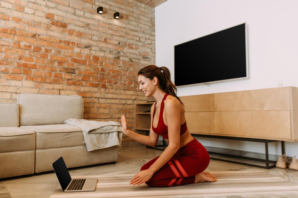 Mutlu kız çevrimiçi yoga minderinde dizüstü bilgisayarla kendini izole etme üzerine eğitim görüyor. - Fotoğraf, Görsel