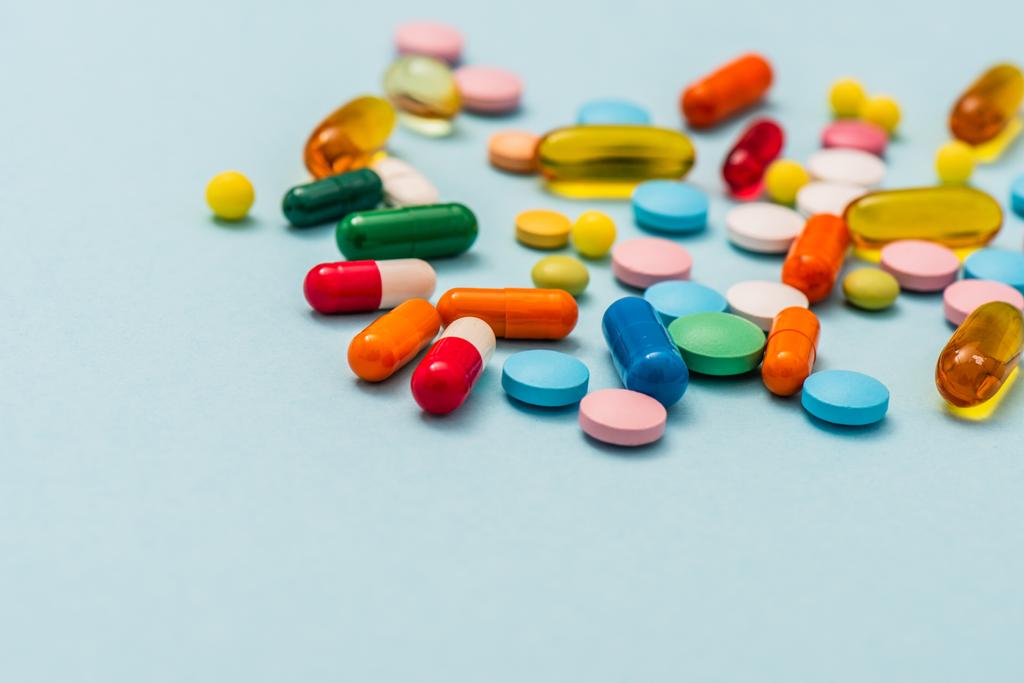 Foco seletivo de pílulas coloridas e cápsulas em fundo azul
 - Foto, Imagem