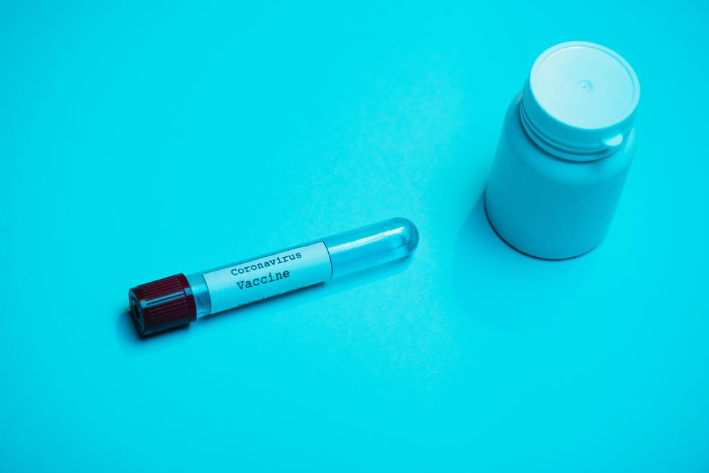 Άποψη υψηλής γωνίας του δοκιμαστικού σωλήνα με το εμβόλιο του κορωναϊού και του δοχείου σε μπλε - Φωτογραφία, εικόνα