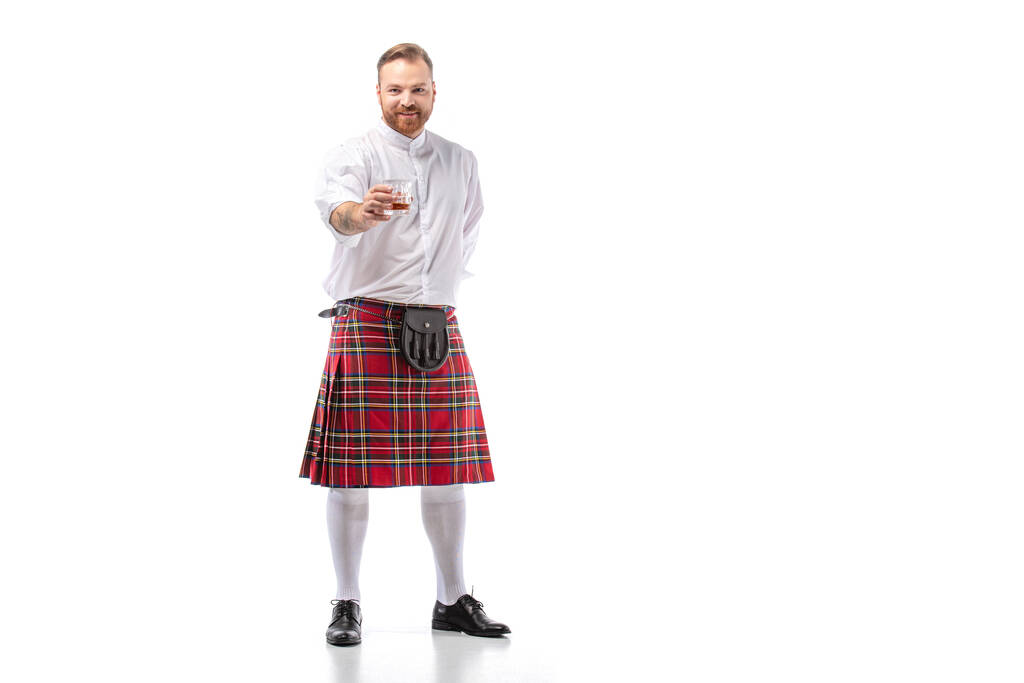 smiling Scottish redhead man in red kilt with whiskey in glass on white background - Photo, Image