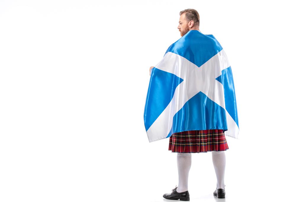 achteraanzicht van Schotse roodharige man in rode kilt met vlag van Schotland op witte achtergrond - Foto, afbeelding