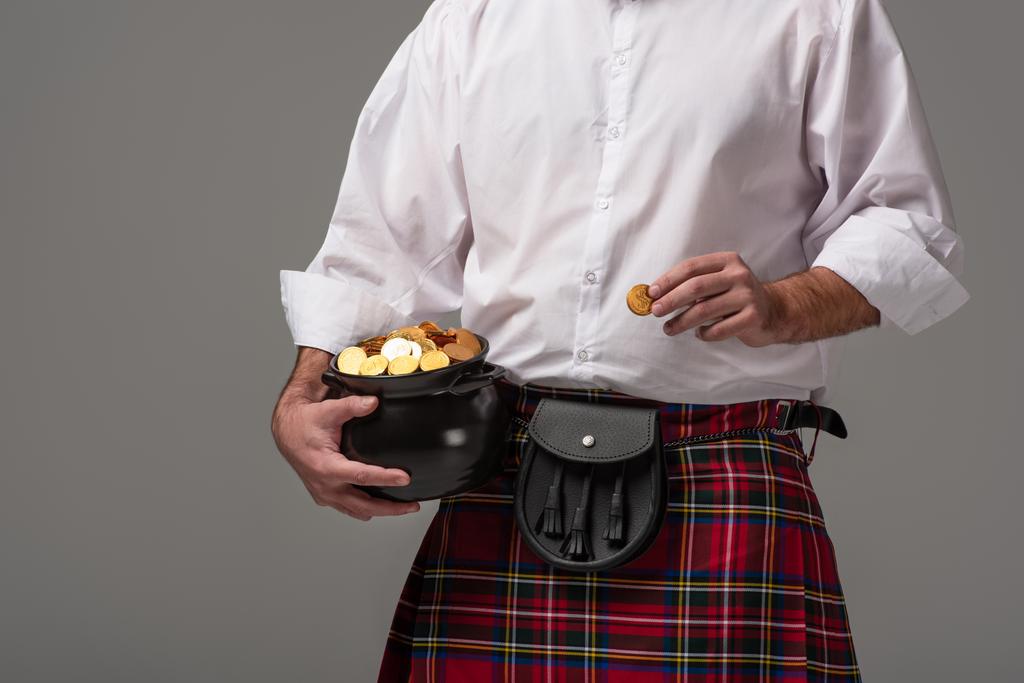 bijgesneden beeld van Schotse man in rode oven met potje met gouden munten op grijze achtergrond - Foto, afbeelding