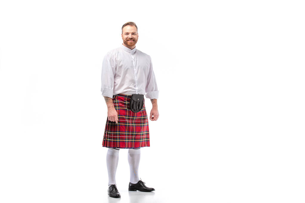Lächelnder schottischer Rotschopf mit Bart in rotem Schottenkilt auf weißem Hintergrund - Foto, Bild
