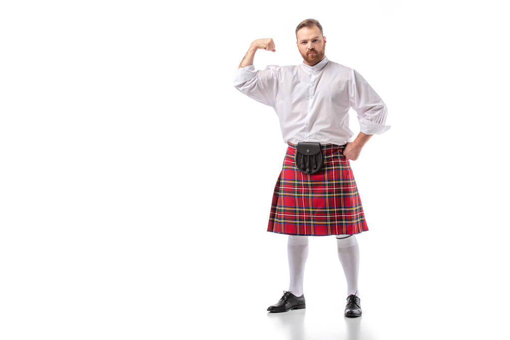 strong Scottish redhead bearded man in red tartan kilt showing biceps on white background - Photo, Image