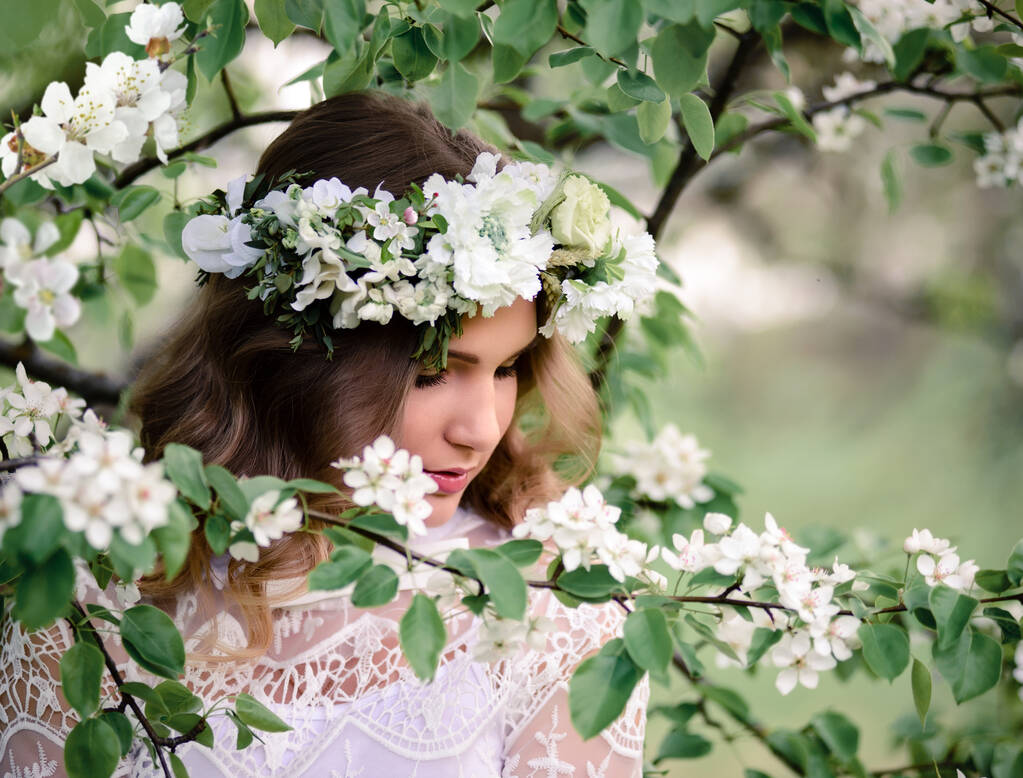 Una mujer hermosa con un vestido blanco cerca de un árbol floreciente. Una joven sobre el fondo de flores de cerezo de primavera. Dama romántica en un jardín floreciente
 - Foto, imagen