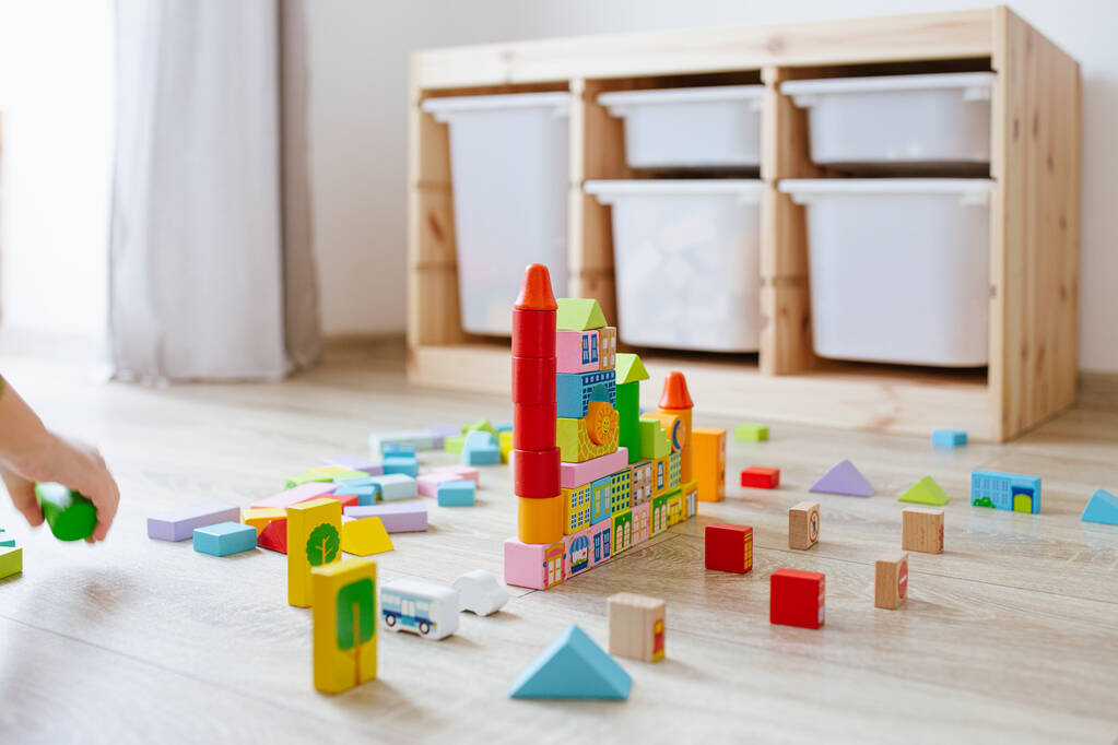Niño irreconocible jugando con bloques de construcción de madera de colores en el suelo en la habitación de los niños. Enfoque selectivo
 - Foto, imagen